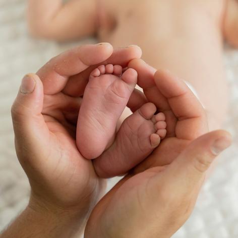 Ein Elternteil hält behutsam die winzigen Füsse eines Babys in den Händen